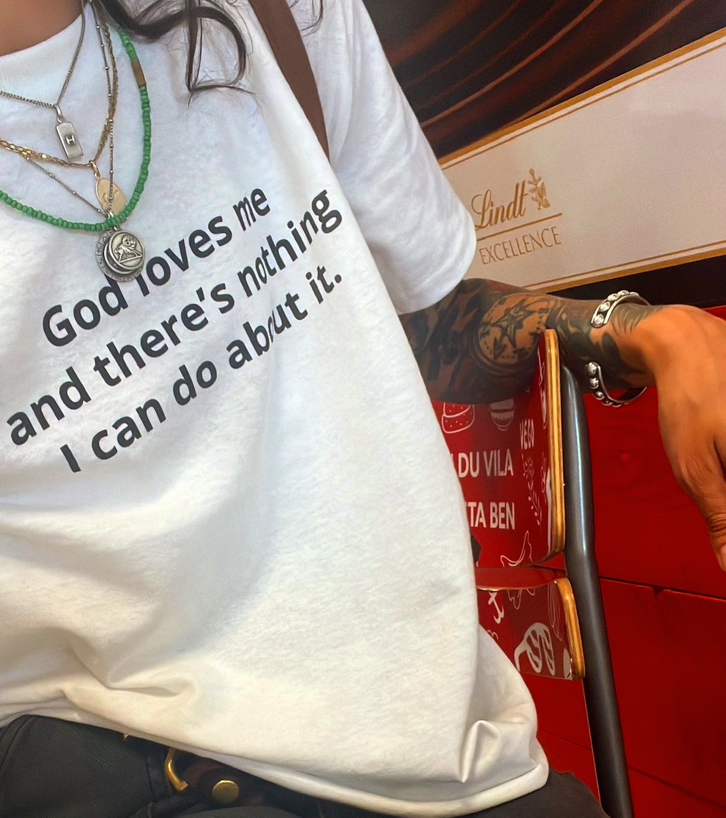 A person wearing a white graphic T-shirt with the text 'God loves me and there's nothing I can do about it.' printed in black.